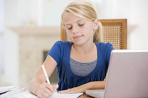 Young Girl Doing Homework And Using Laptop
