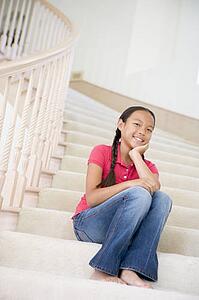 Young Girl Sitting On A Stairwell At Home