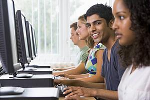 Four people sitting at computer terminals (selective focus/high key)