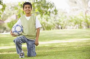 Young boy outdoors at park holding ball and smiling (selective focus)