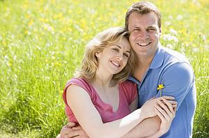 Couple sitting outdoors holding flower smiling
