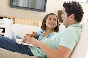 Man with young girl in living room with laptop smiling