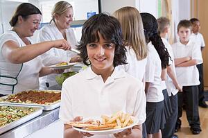 Students in cafeteria line with one holding his unhealthy meal and looking at camera (depth of field)