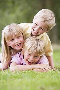 Three young children playing outdoors smiling