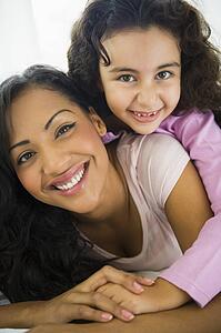 Mother and daughter in living room embracing and smiling (high key/selective focus) 