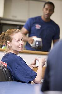 Three firefighters in break room with one getting coffee in background (selective focus)
