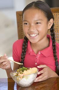 Young girl in dining room eating Chinese food smiling