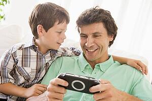 Man and young boy with handheld game smiling