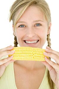 Teenage girl holding corn on cob and smiling