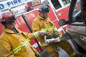 Two firemen using the jaws of life on a car door
