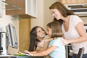 Woman and two young girls in kitchen with computer smiling