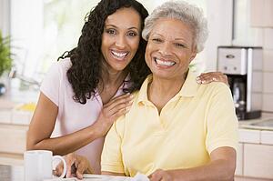 Two women in kitchen with newspaper and coffee smiling