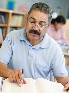 Man sitting in library with a book and notepad (selective focus)