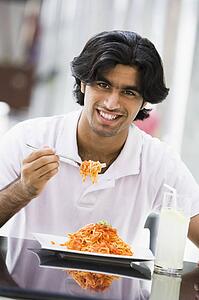 Man at restaurant eating spaghetti and smiling (selective focus)
