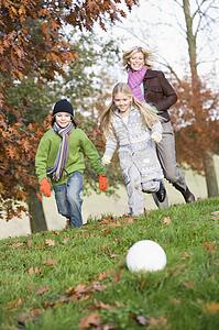 Mother outdoors in park with two young children playing soccer and smiling (selective focus)