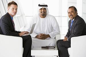 Three businessmen indoors with a laptop smiling (high key/selective focus)