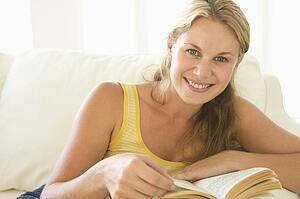 Woman in living room reading book smiling
