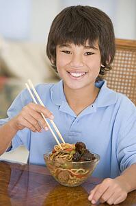 Young boy in dining room eating chinese food smiling