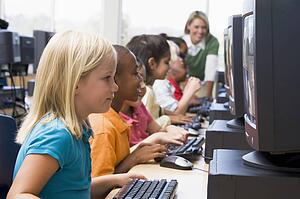 Children at computer terminals with teacher in background (depth of field/high key)