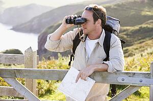 Man relaxing on cliffside path holding map and binoculars