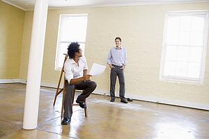 Man sitting on ladder in empty space holding paper talking to other man