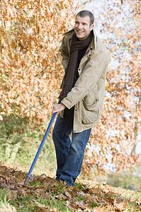Man outdoors raking leaves and smiling (selective focus)