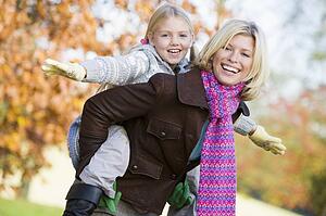 Mother outdoors piggybacking daughter and smiling (selective focus)