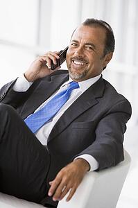 Businessman sitting indoors on cellular phone smiling (high key/selective focus)