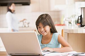 Young girl in kitchen with laptop and paperwork smiling with woman in background