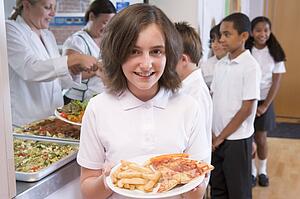 Students in cafeteria line with one holding unhealthy meal looking at camera (depth of field)