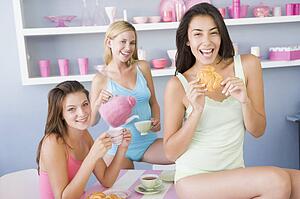 Three young woman sitting at a table having tea and a snack