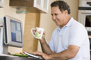 Man in kitchen with computer and coffee smiling