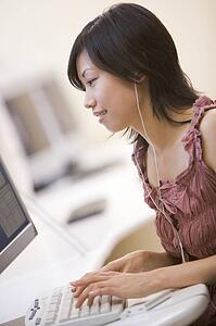 Woman in computer room listening to MP3 player while typing and smiling