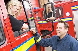 Firewoman sitting in fire engine talking to fireman standing outside