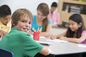 Students in class writing with teacher in background (selective focus)