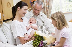 New mother with baby and family in hospital smiling