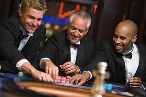 Three men in casino playing roulette smiling (selective focus)
