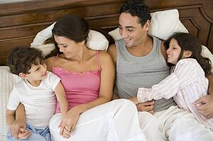 Family relaxing on bed in bedroom smiling (selective focus)