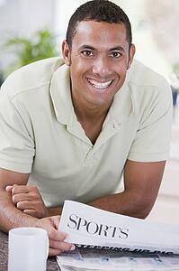 Man in kitchen reading newspaper and smiling