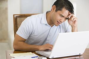 Man in dining room using laptop and frowning