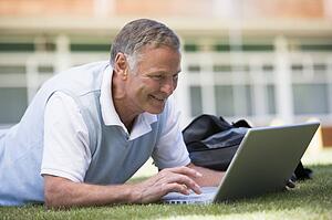 Man lying on lawn of school with laptop