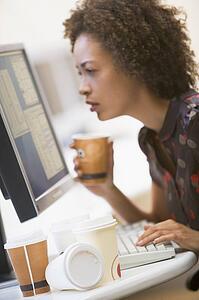 Woman in computer room with many cups of empty coffee around her