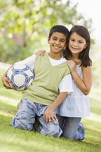 Two young children outdoors in park with ball smiling (selective focus)
