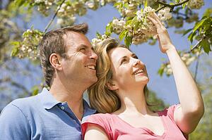 Couple standing outdoors holding blossom smiling