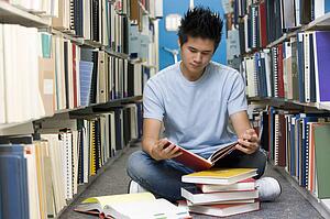 Man sitting on floor in library reading book