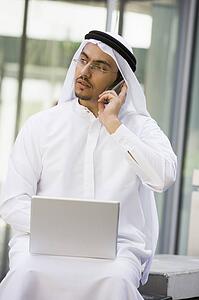 Businessman outdoors with laptop using cellular phone by building (selective focus)