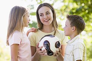 Woman and two young children outdoors holding volleyball and smiling