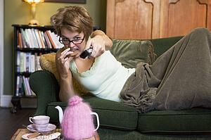 Young woman lying on sofa at home eating cookies and watching television