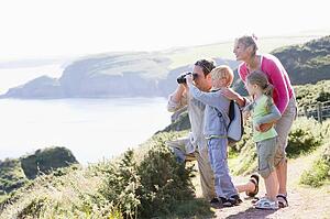 Family on cliffside path using binoculars and smiling