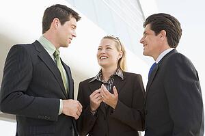 Three businesspeople standing outdoors by building talking and smiling